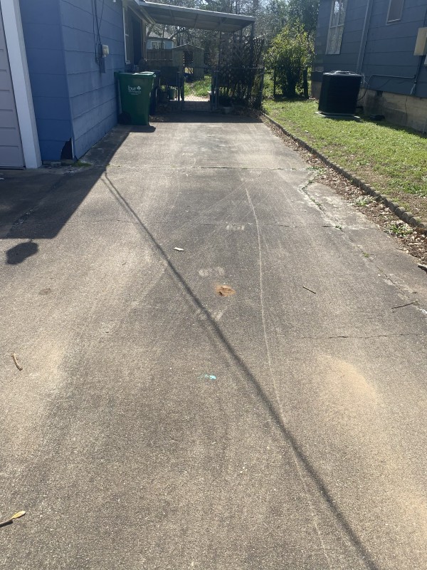 Long residential concrete driveway with dirt and tire marks before pressure washing